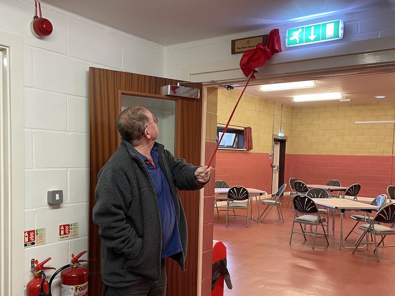 Brian Spray removing a small curtain to unveil the hall's new plaque